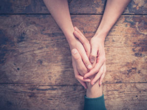 Close up on a man and a woman holding hands at a wooden table